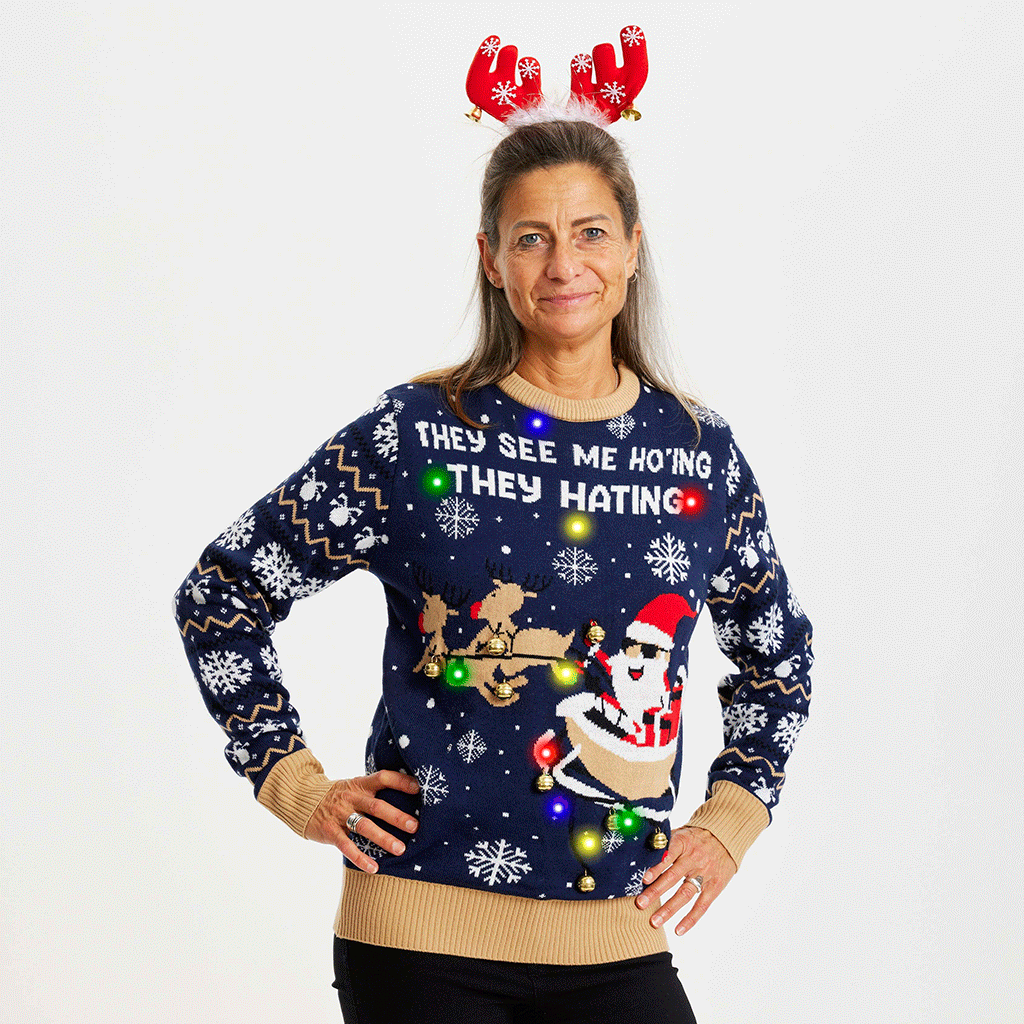 Une femme, les mains le long du corps, portant un pull de Noël jaune et bleu avec la citation